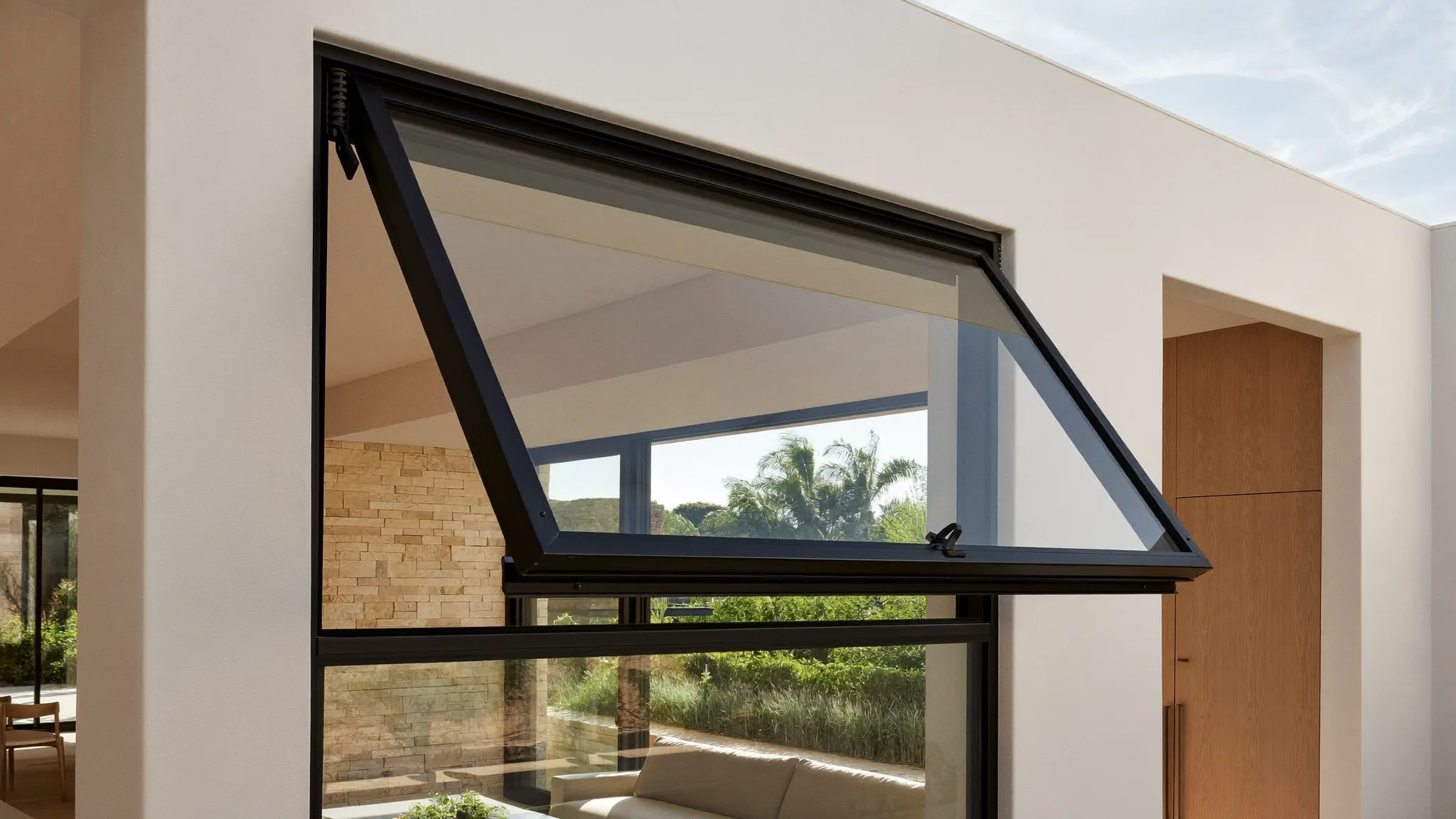Close-up of a black-framed awning window cranked open outward on a modern home, with lush greenery outside